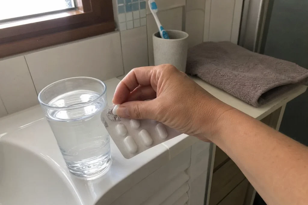 En hand trycker ut en metformintablett ur en blisterförpackning bredvid ett vattenglas på badrumsbänken.