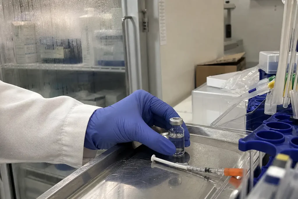 En handskbeklädd hand placerar en injektionsflaska på en labbricka, inför att nytt ebolavaccin ska testas på människor.