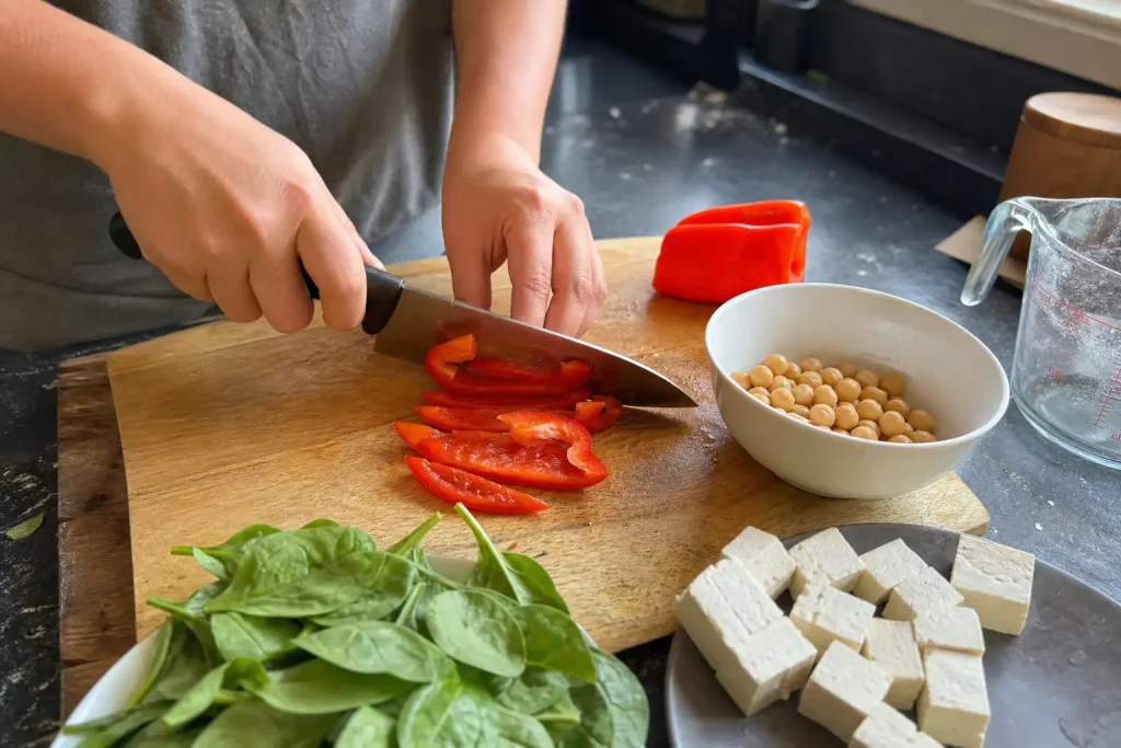 Ett par händer skär rödpaprika vid ett köksbord med kikärtor, tofu och spinat, del av jakten på nyttigare järnrik mat