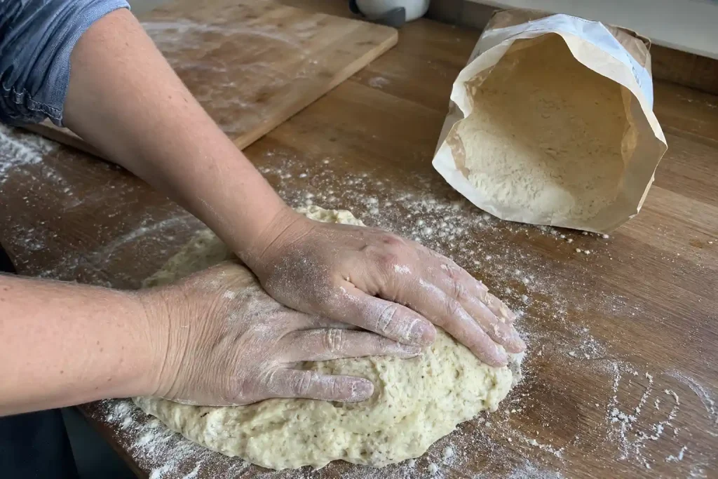 Mjölade händer knådar löst degen till ett lchf recept vid köksbänken en vardagseftermiddag.